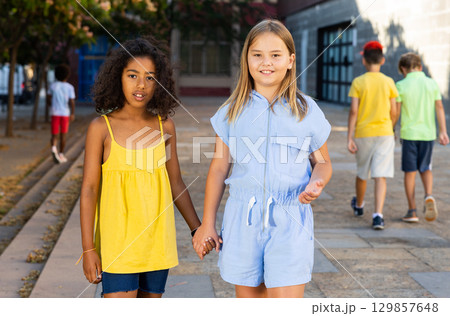 Positive girls walking together through alley during summer day Positive girls walking together through alley during summer day 129857648