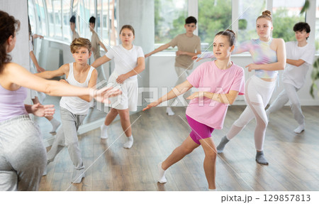 Young girls and boys repeat the movements of dance teacher, training in spacious studio Young girls and boys repeat the movements of dance teacher, training in spacious studio 129857813