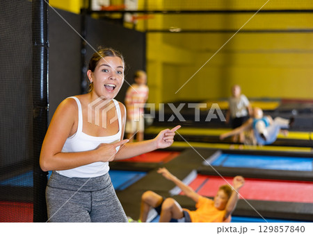 Happy young European female in white top and gray leggings posing on trampolines during active weekend free time in entertainment center Happy young European female in white top and gray leggings posing on trampolines during active weekend free time in entertainment center 129857840