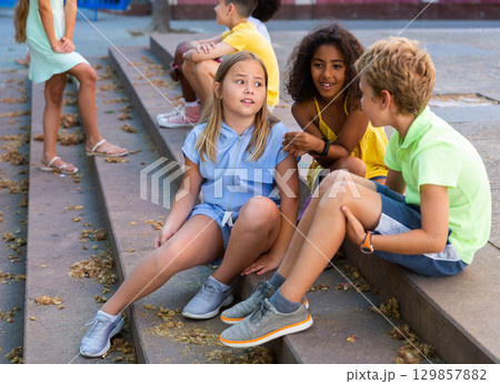 Children talking together while sitting on stairs outdoors Children talking together while sitting on stairs outdoors 129857882