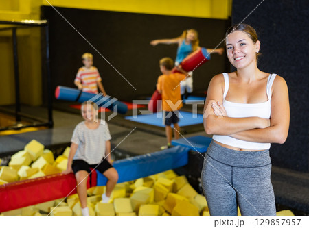 Portrait of happy young European female in white top and gray leggings posing on trampolines foam cube pool in amusement center Portrait of happy young European female in white top and gray leggings posing on trampolines foam cube pool in amusement center 129857957