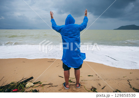 back of male tourist in a raincoat on dirty beach by the sea after a storm in cloudy weather. Concept of the rainy and monsoon season 129858530