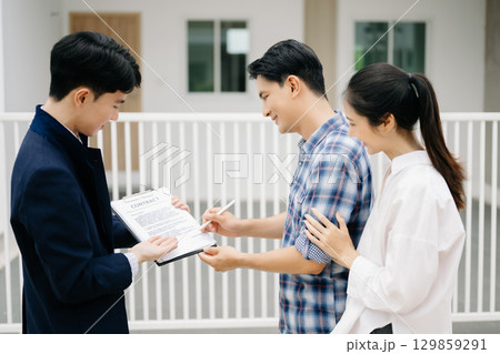 Asian man Real estate broker agent showing a house detail in her file to the young Asian couple lover looking and interest to buy it. 129859291