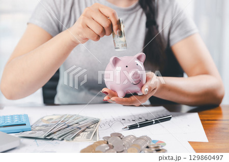 Businesswoman saving money with piggy bank and coins on desk, financial planning and investment concept. Young Asian woman making stack of coin. invest save finance concept, saving money, investment 129860497
