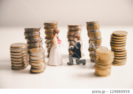 Save money for wedding and planning wedding concept. Sustainable financial goal for family life or married life. Miniature wedding on rows of rising coins, depicts savings or growth for new family. 129860959