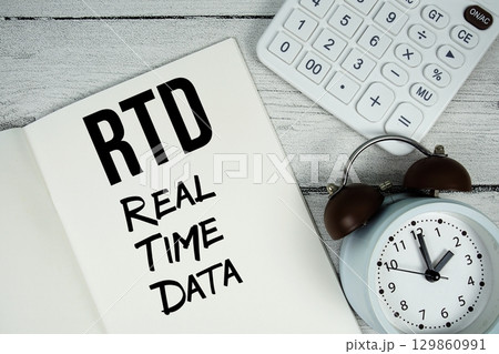 RTD Real Time Data text on paper notebook page with alarm clock and calculator on wooden background 129860991