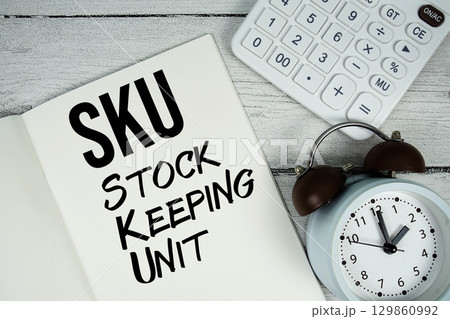 SKU Stock Keeping Unit text on paper notebook page with alarm clock and calculator on wooden background 129860992