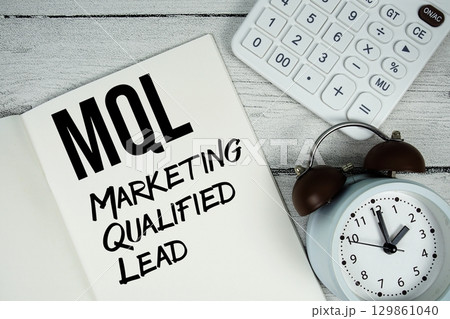 MQL Marketing Qualified Lead text on paper notebook page with alarm clock and calculator on wooden background 129861040