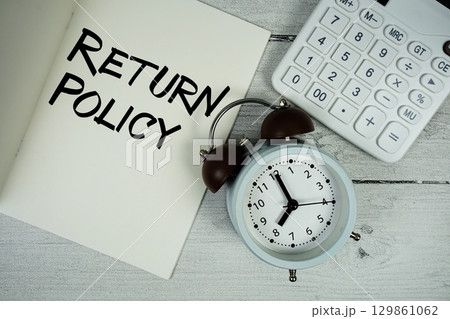 Return Policy text on paper notebook page with alarm clock and calculator on wooden background 129861062