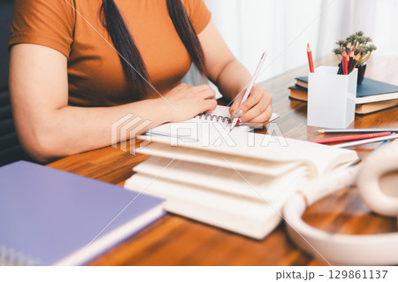 woman sitting at desk working on laptop taking notes in notebook, female studying online, watching webinar using computer, writing check list. Remote college school education, e learning concept. woman sitting at desk working on laptop taking notes in notebook, female studying online, watching webinar using computer, writing check list. Remote college school education, e learning concept. 129861137