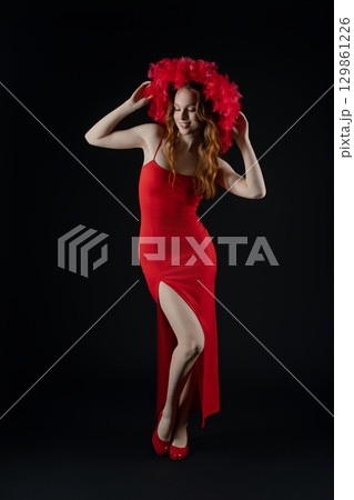 Woman in a red dress and feathered hat poses expressively in a studio setting showcasing confidence and emotion 129861226