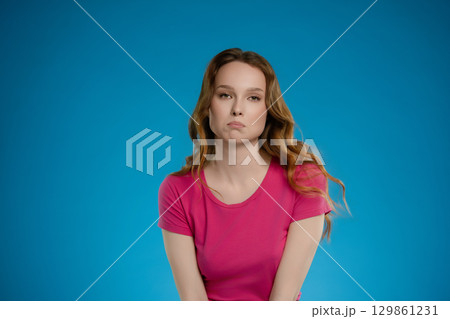 Woman with wavy hair posing in a studio setting expressing emotion against a vibrant blue background 129861231