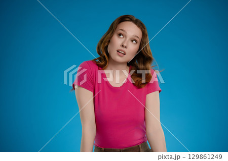 Woman posing in studio with expressive emotion against vibrant blue background while showcasing a playful demeanor Woman posing in studio with expressive emotion against vibrant blue background while showcasing a playful demeanor 129861249
