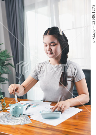 Businesswoman saving money with piggy bank and coins on desk, financial planning and investment concept. Young Asian woman making stack of coin. invest save finance concept, saving money, investment 129861278