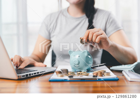 Businesswoman saving money with piggy bank and coins on desk, financial planning and investment concept. Young Asian woman making stack of coin. invest save finance concept, saving money, investment Businesswoman saving money with piggy bank and coins on desk, financial planning and investment concept. Young Asian woman making stack of coin. invest save finance concept, saving money, investment 129861280