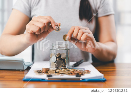 Businesswoman saving money with piggy bank and coins on desk, financial planning and investment concept. Young Asian woman making stack of coin. invest save finance concept, saving money, investment Businesswoman saving money with piggy bank and coins on desk, financial planning and investment concept. Young Asian woman making stack of coin. invest save finance concept, saving money, investment 129861281