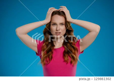 Woman expressing complex emotions while posing in a studio with a vibrant blue background 129861302