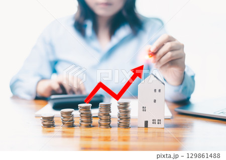 Stacks of coins with glowing house icon and upward arrows, symbolizing real estate investment growth. House shape cardboard with free copy space for your creativity ideas text. Finance concept. 129861488
