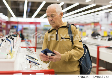elderly man examines tablet computer in showroom of electronics store 129861738
