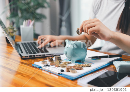 Businesswoman saving money with piggy bank and coins on desk, financial planning and investment concept. Young Asian woman making stack of coin. invest save finance concept, saving money, investment Businesswoman saving money with piggy bank and coins on desk, financial planning and investment concept. Young Asian woman making stack of coin. invest save finance concept, saving money, investment 129861991