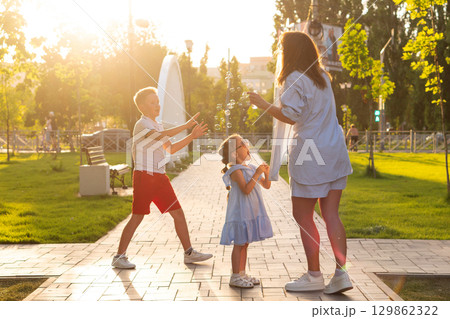 Boy and girl reach bubbles while mother blows Boy and girl reach bubbles while mother blows 129862322