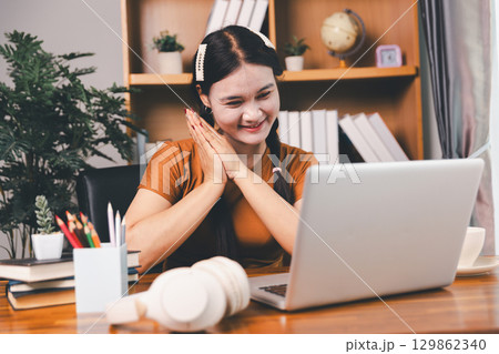 Asian girl doing homework and studying at home. woman using laptop at desk write notes watching webinar, study online, look at learn web class or having virtual call meeting remote working from home. Asian girl doing homework and studying at home. woman using laptop at desk write notes watching webinar, study online, look at learn web class or having virtual call meeting remote working from home. 129862340