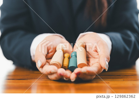 Hands protecting family wooden model for insurance and assurance life concept. Businessman hand gesture protecting wooden domino falling to family dolls for insurance and assurance. 129862362