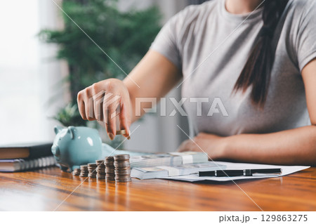 Businesswoman saving money with piggy bank and coins on desk, financial planning and investment concept. Young Asian woman making stack of coin. invest save finance concept, saving money, investment 129863275