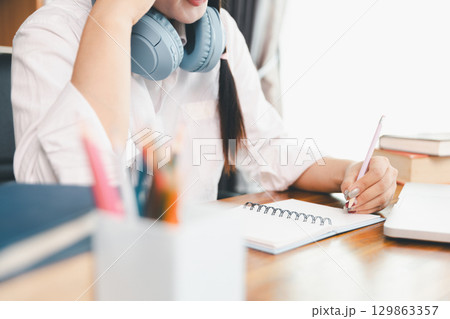 Asian girl student wear headphones learning online watching webinar class looking at laptop computer eLearning remote lesson making notes or video calling virtual conference meeting teacher at home. Asian girl student wear headphones learning online watching webinar class looking at laptop computer eLearning remote lesson making notes or video calling virtual conference meeting teacher at home. 129863357