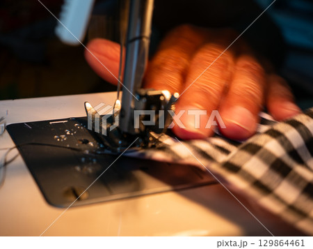 Elderly Woman Hands Sewing Fabric with Electric Sewing Machine. Senior Labor and Handicraft Work. 129864461