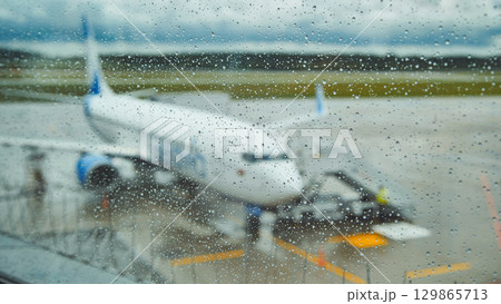 Raindrops blurring airplane view while parked on wet airport tarmac during rainfall Raindrops blurring airplane view while parked on wet airport tarmac during rainfall 129865713