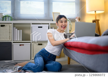 Excited young woman celebrating success while working on laptop at home 129866072
