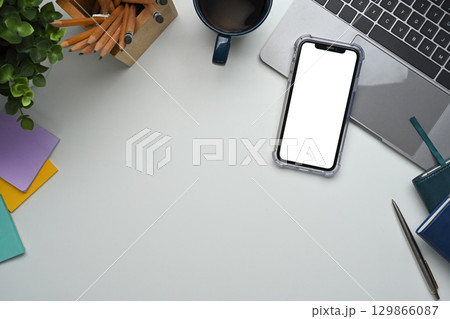 Blank screen smartphone, laptop, coffee cup, and office supplies on white desk Blank screen smartphone, laptop, coffee cup, and office supplies on white desk 129866087
