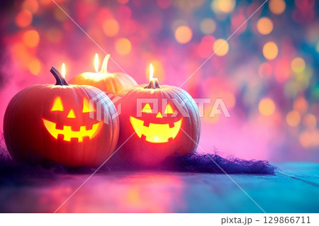 Candle lit Halloween pumpkins glowing in vibrant colors with empty space for festive greetings 129866711