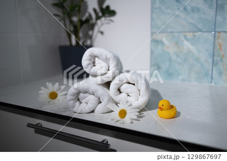 Soft Rolled Towels With Flowers and a Rubber Duck on a Bathroom Counter 129867697