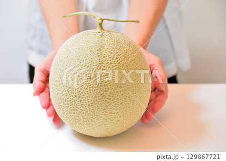 マスクメロン（熊本県産）をどうぞと差し出す女性 129867721