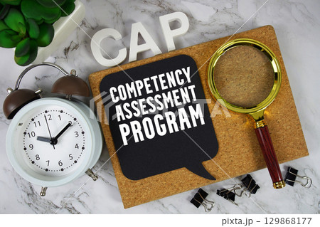 CAP Competency Assessment Program text with alarm clock and magnifying glass on marble background 129868177