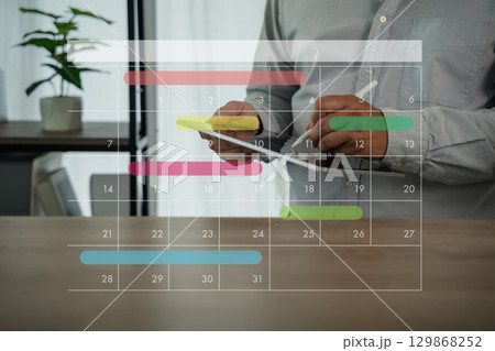Business person using digital planner on smartphone and computer with monthly calendar overlay, planning schedule, organizing tasks, and managing time for productivity in modern office. Business person using digital planner on smartphone and computer with monthly calendar overlay, planning schedule, organizing tasks, and managing time for productivity in modern office. 129868252