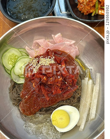 Naengmyeon, a refreshing Korean cold noodle dish served in an icy broth, topped with sliced vegetables, a boiled egg, and spicy sauce. Perfect for summer food photography and Korean cuisine projects. Naengmyeon, a refreshing Korean cold noodle dish served in an icy broth, topped with sliced vegetables, a boiled egg, and spicy sauce. Perfect for summer food photography and Korean cuisine projects. 129868982