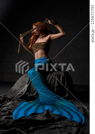 Young mermaid holding cloth in dark studio Young mermaid holding cloth in dark studio 129871791