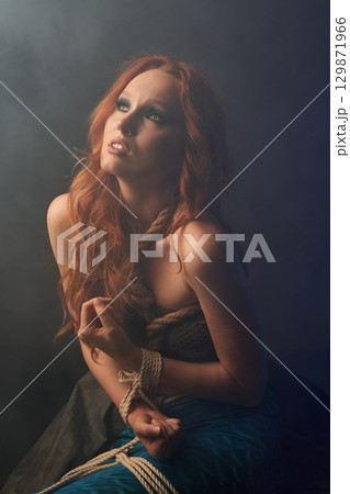 Frightened redheaded mermaid tied with ropes 129871966