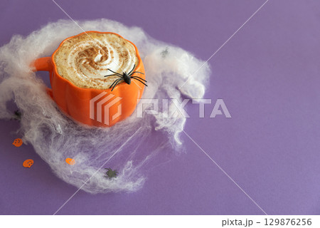 Halloween themed flat lay with a pumpkin latte and spiderwebs on a purple background. Halloween themed flat lay with a pumpkin latte and spiderwebs on a purple background. 129876256