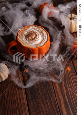 Halloween pumpkin latte with whipped cream and spooky decor on a wooden background. 129876259