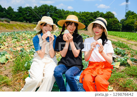 夏の高原で麦わら帽子をかぶった日本人の女の子たちが白いおにぎりを持って座る 129876642