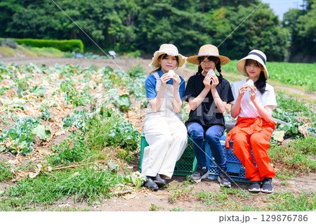 夏の高原で麦わら帽子をかぶった日本人の女の子たちが白いおにぎりを持って座る 129876786