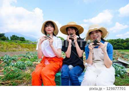 夏の高原で麦わら帽子をかぶった日本人の女の子たちが白いおにぎりを持って座る 129877701