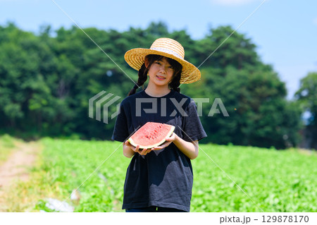 夏の高原で麦わら帽子をかぶった小学生の女の子がスイカを持つ風景 夏の高原で麦わら帽子をかぶった小学生の女の子がスイカを持つ風景 129878170