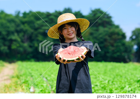 夏の高原で麦わら帽子をかぶった小学生の女の子がスイカを持つ風景 129878174