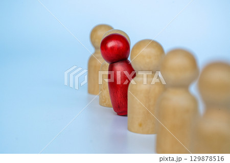 A red wooden figure stands between beige figures, symbolizing courage to speak up in leadership, bullying, or harassment 129878516