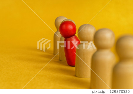 A red wooden figures apart from beige figures on yellow background, symbolizing speaking truth despite isolation in leadership or harassment 129878520
